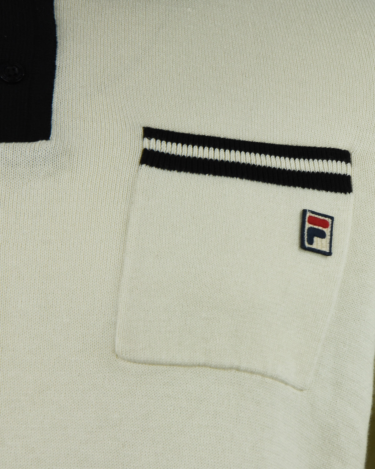 Cream polo chest pocket with black-and-white stripe trim and Fila logo patch.