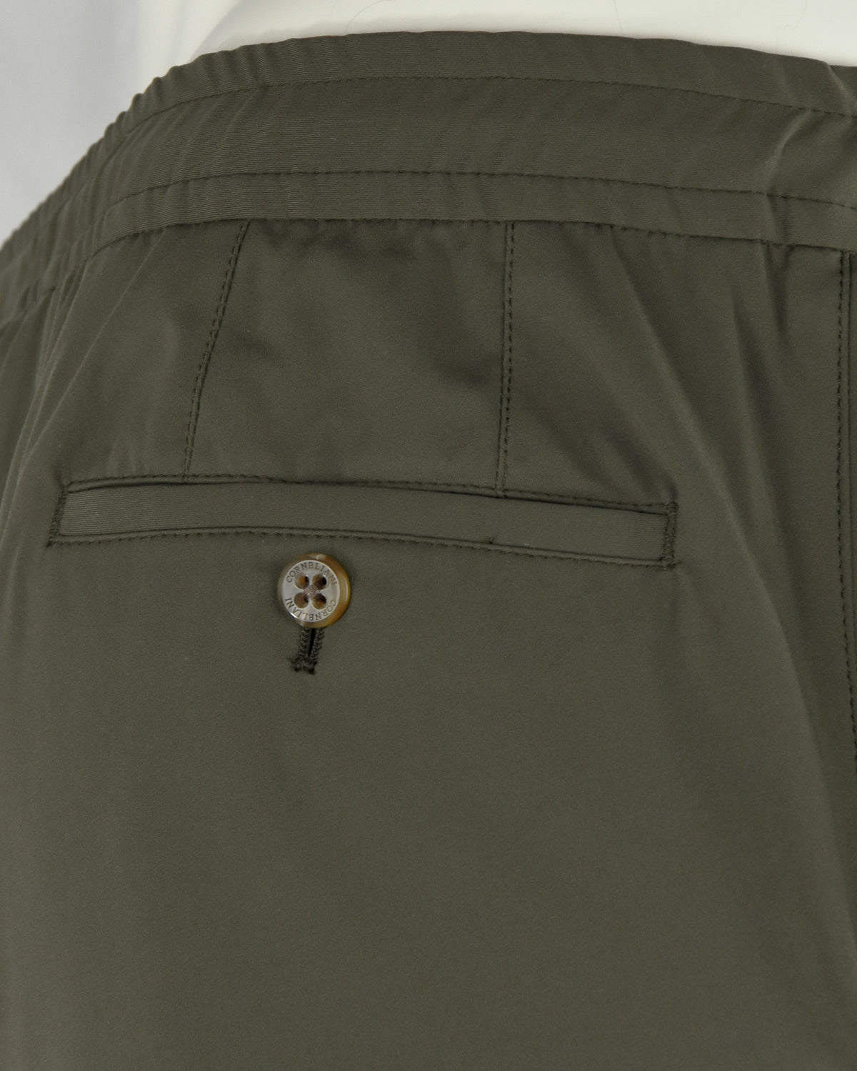 Olive pants close-up: front welt pocket and decorative metal-button closure