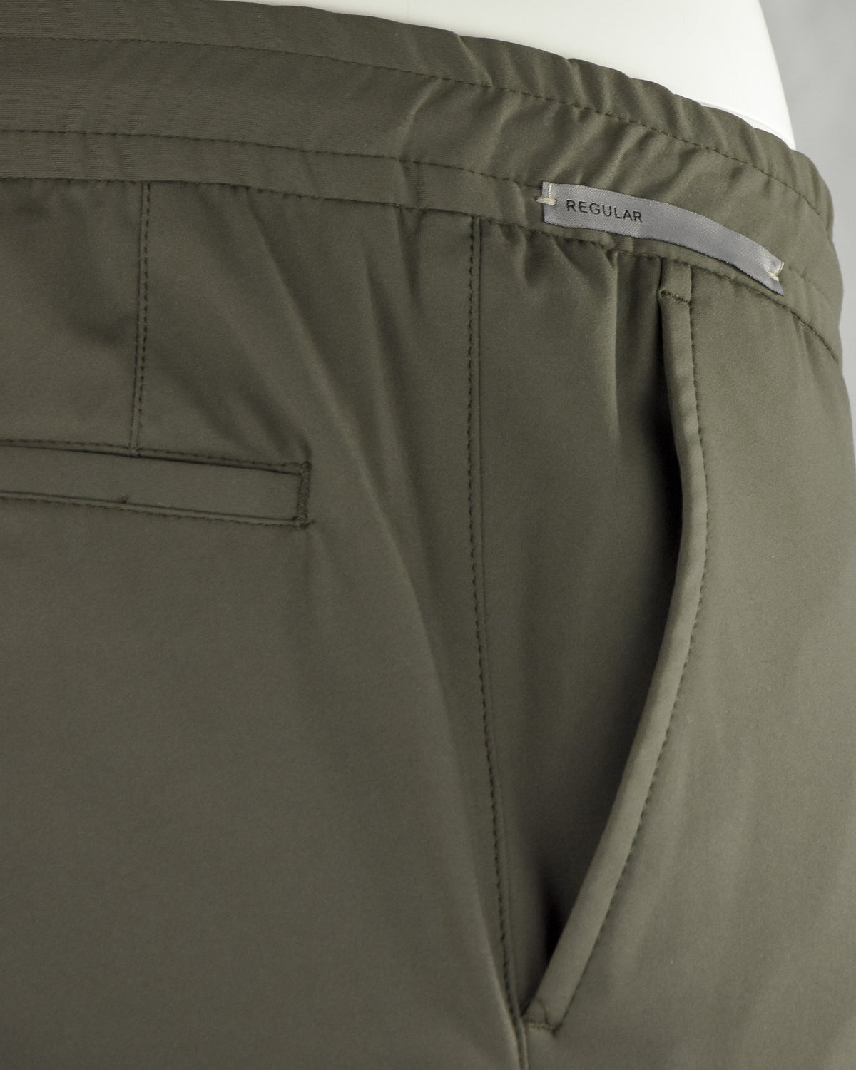 Olive pants close-up: 'REGULAR' label and side pocket seam with welt detailing