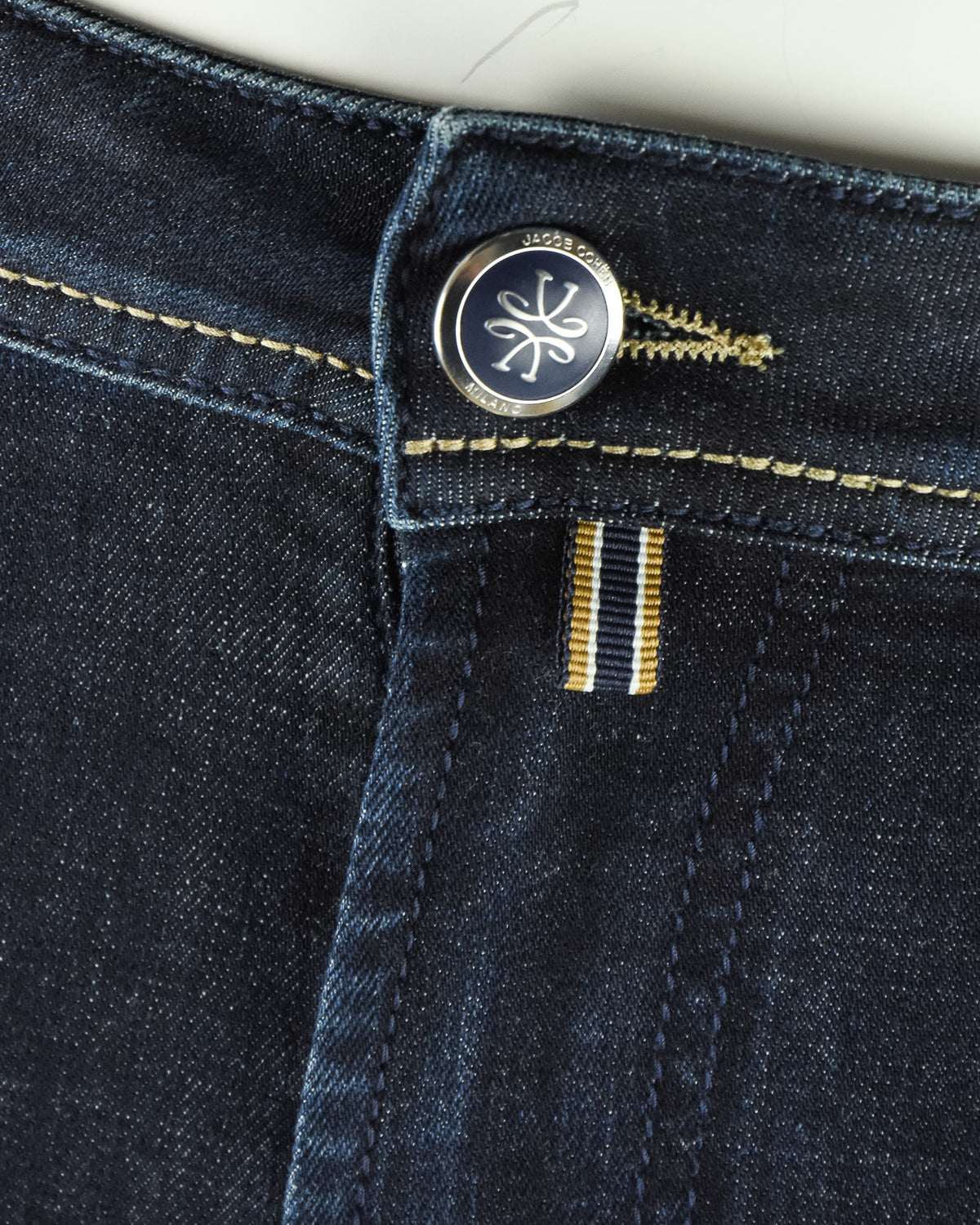 Jeans button closure with circular logo and two gold thread bar details.