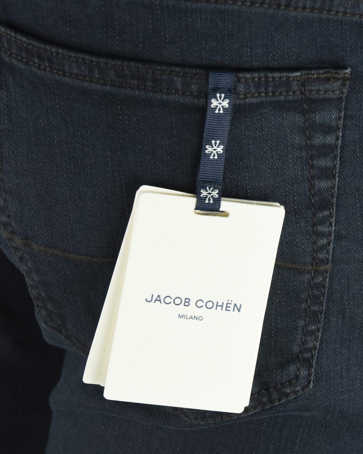 Jacob Cohen size tag hanging from dark blue denim jeans pocket detail.