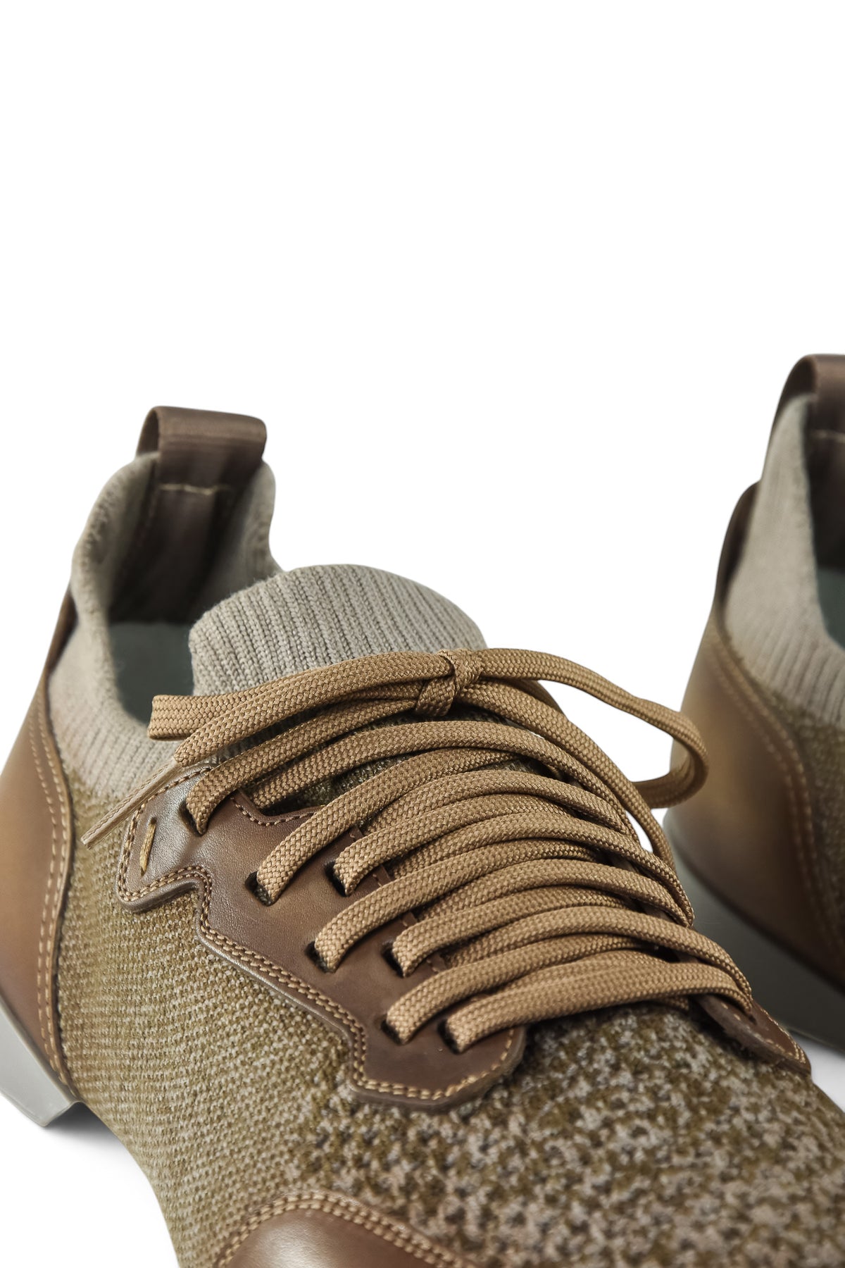 Close-up of tan lace-up knit trainer with brown leather lace placket and textured upper