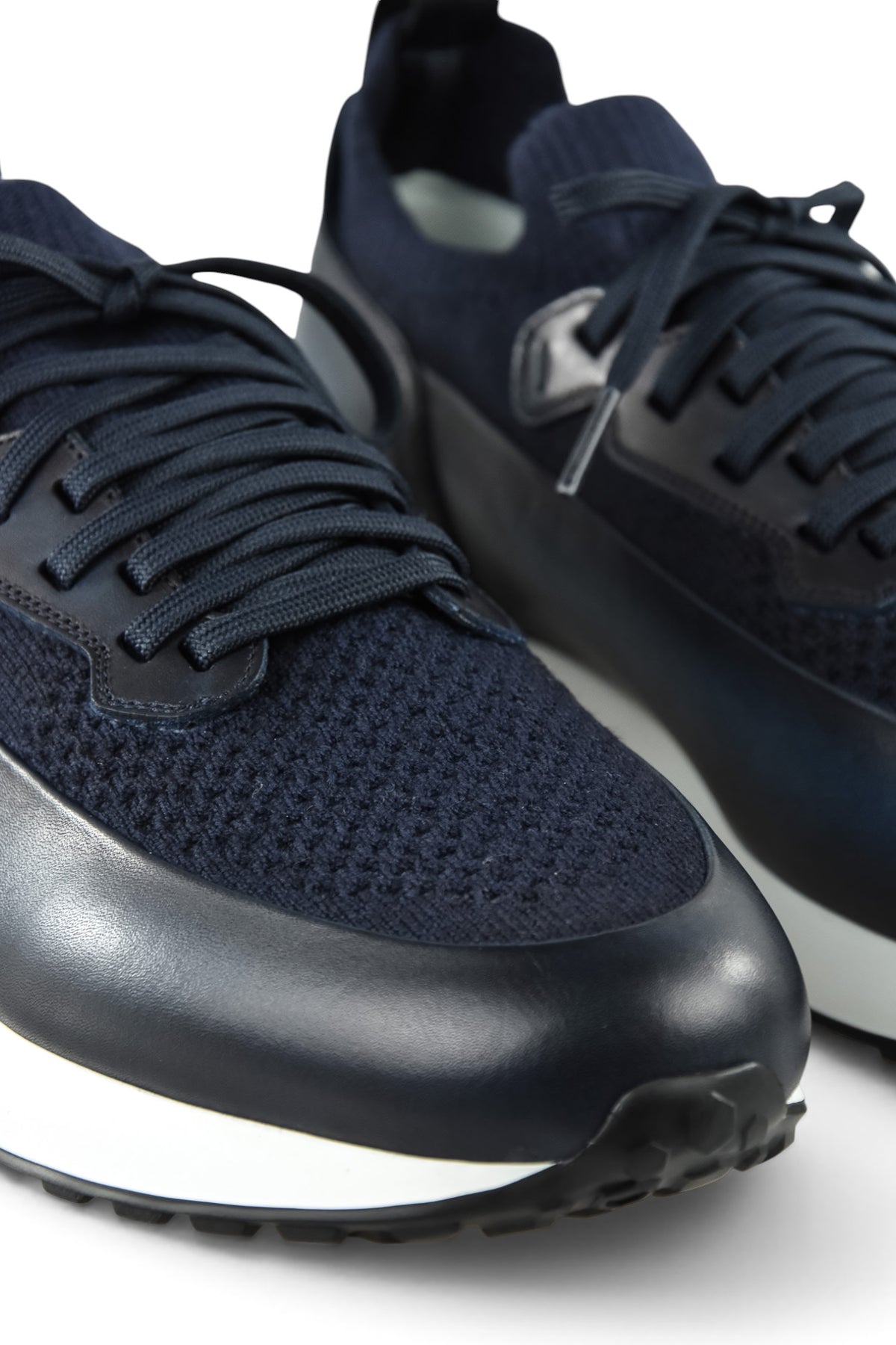 Close-up of dark blue lace-up trainers with knit upper and leather toe and side panels