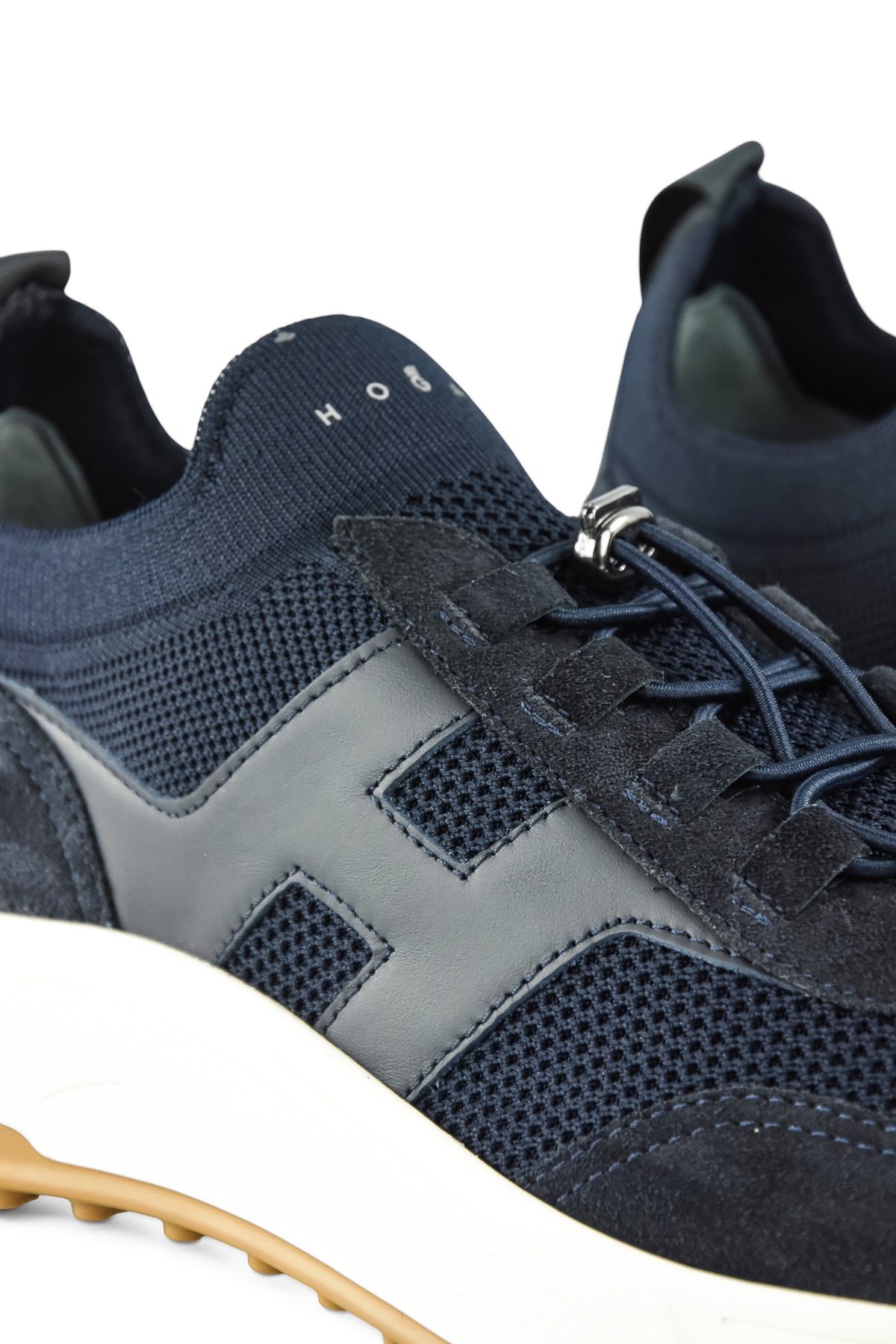 Navy trainer sneaker close-up with perforated knit panels and silver lace eyelets