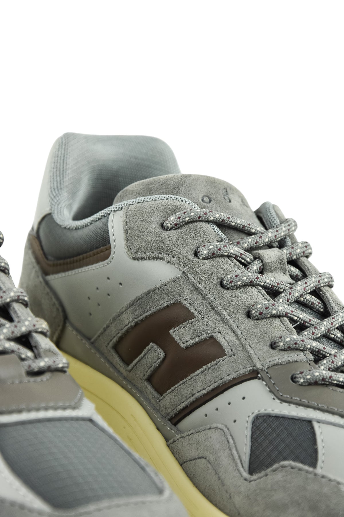 Close-up of grey sneaker upper with textured trim, lace eyelets, and thick light midsole