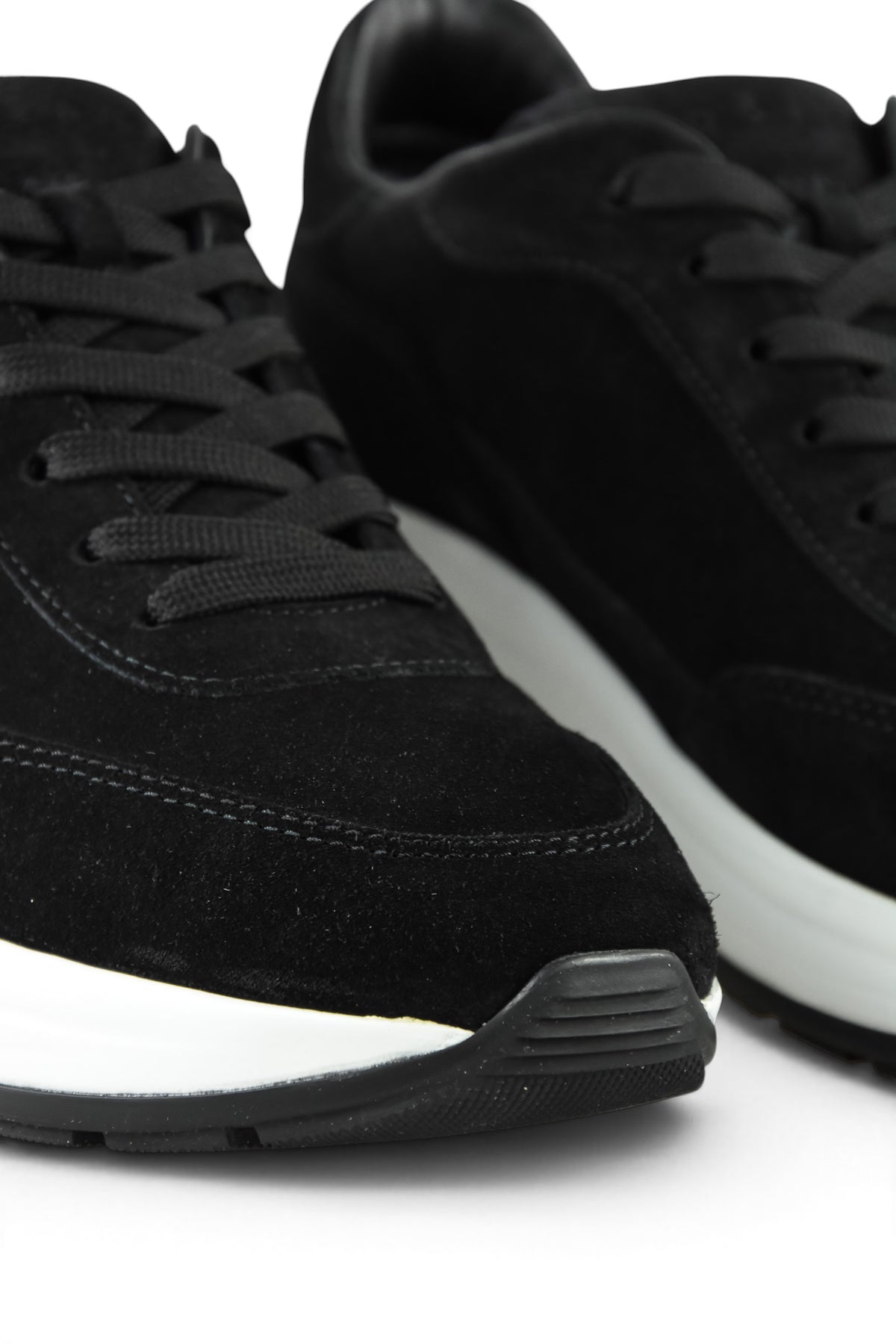 Close-up of black suede lace-up trainers with white midsole and tread