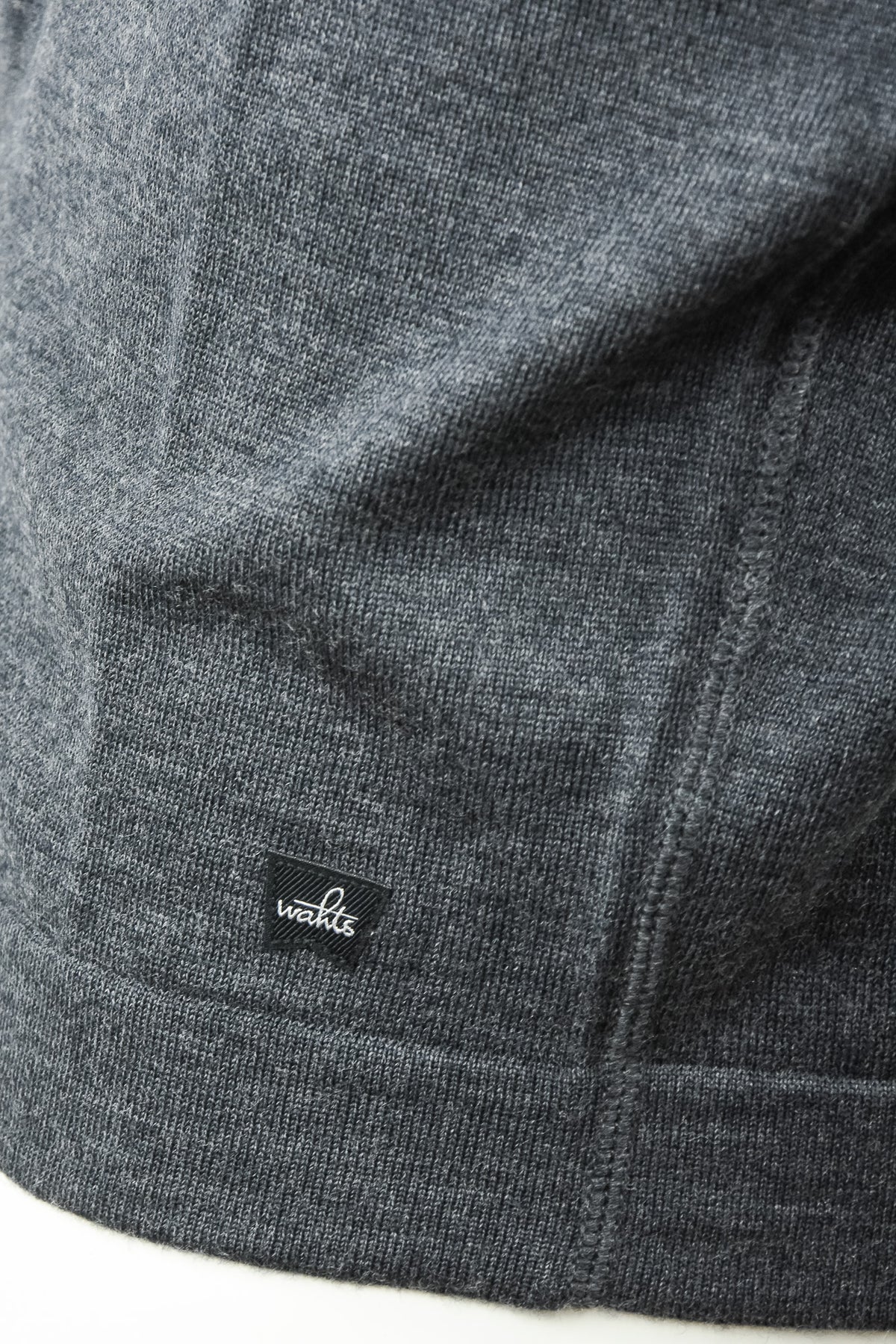 Close-up of the cardigan's merino knit, hem stitching, and WAHTS logo tab