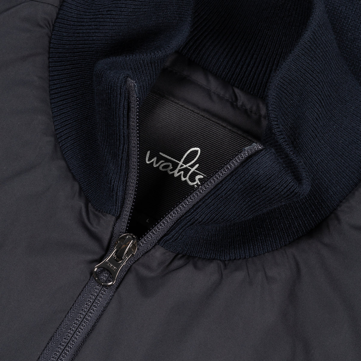 Close-up of WAHTS tag and metal zipper on ribbed knit collar of hybrid jacket.