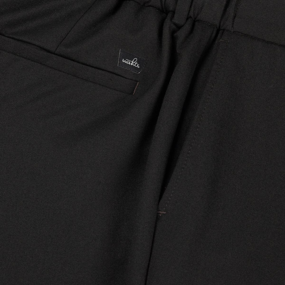 Soft wool travel trousers detail: WAHTS logo label and fabric fold
