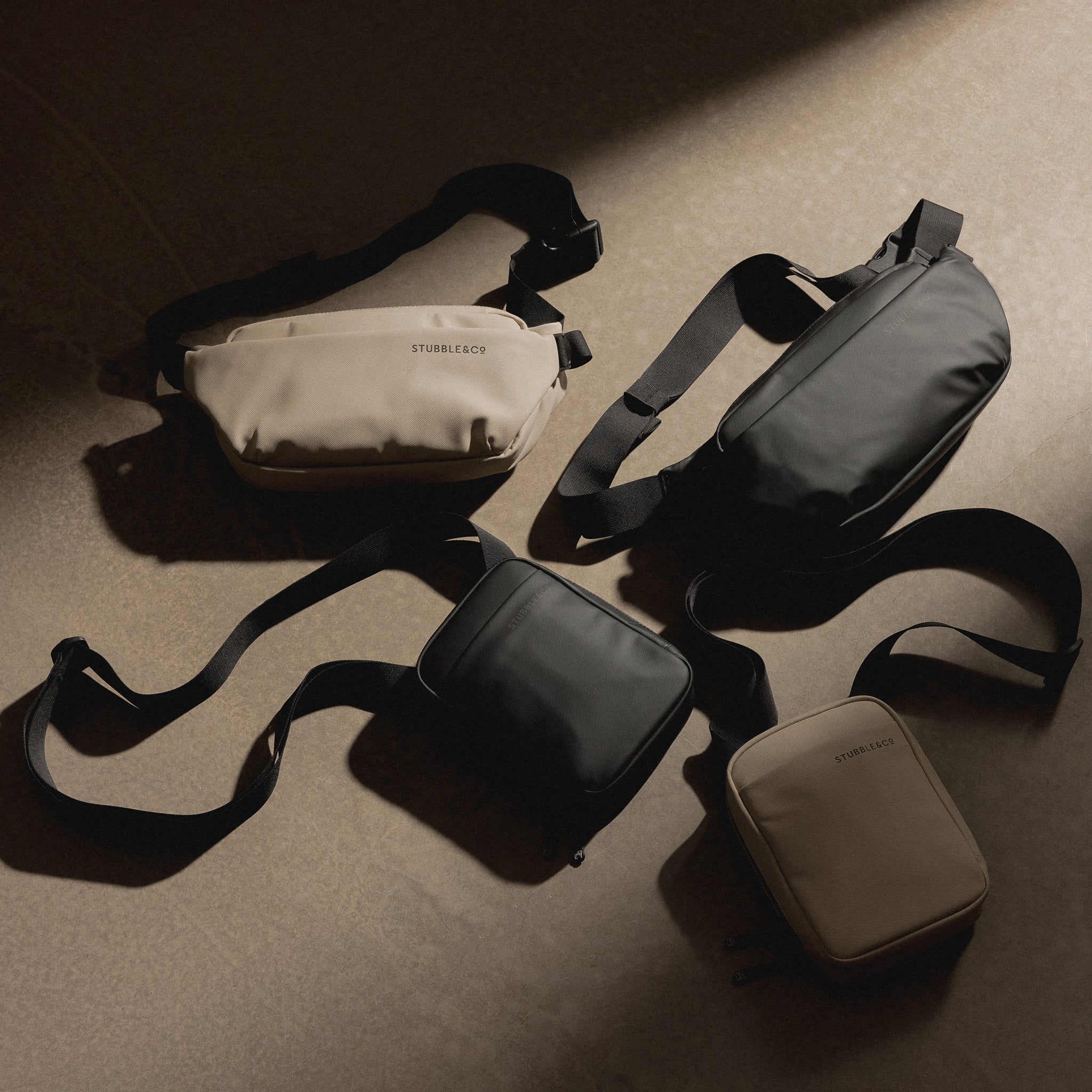 Sand crossbody bag with black webbing strap and zippered front pocket, laid on floor