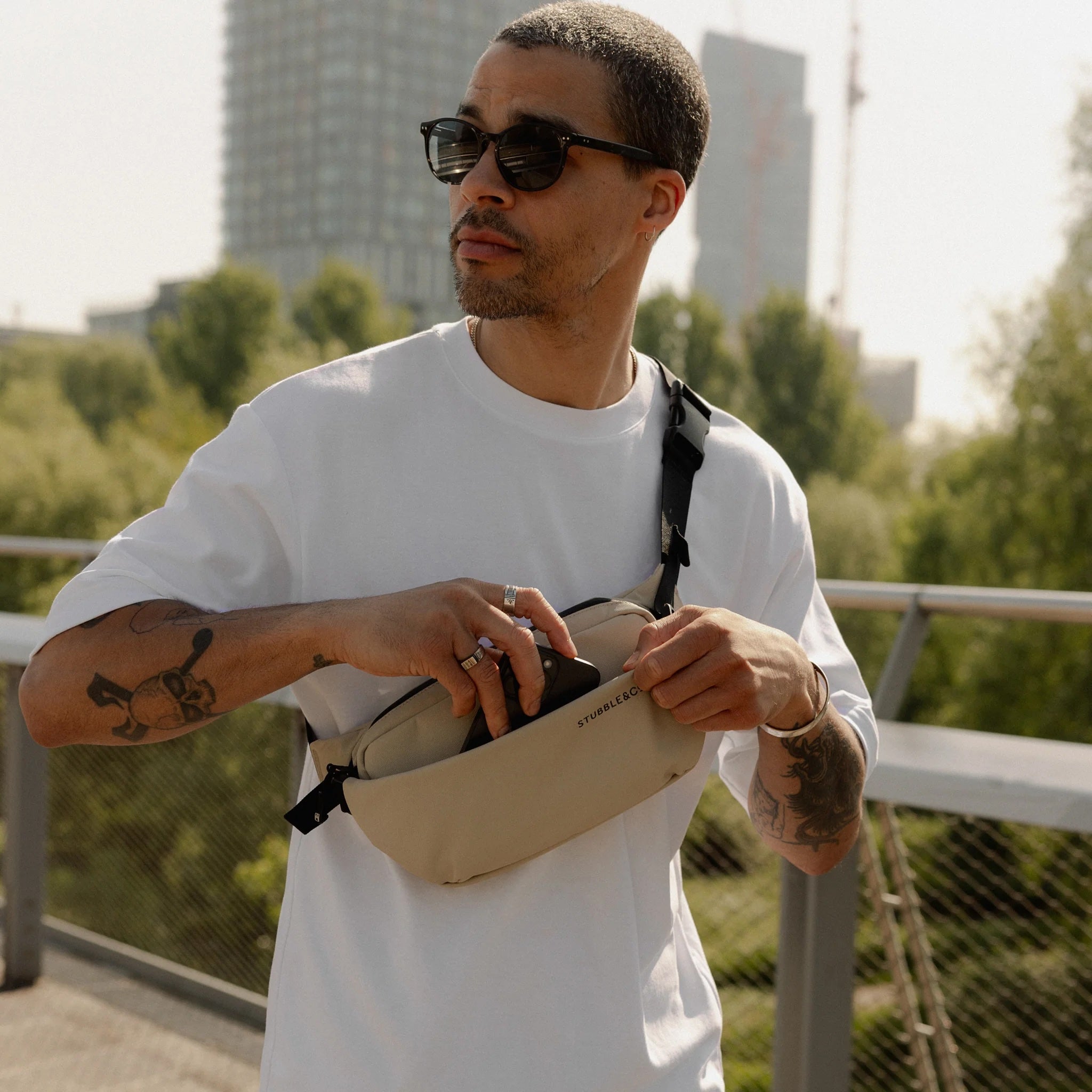 Sand crossbody bag worn across chest with black webbing strap and zippered main pocket