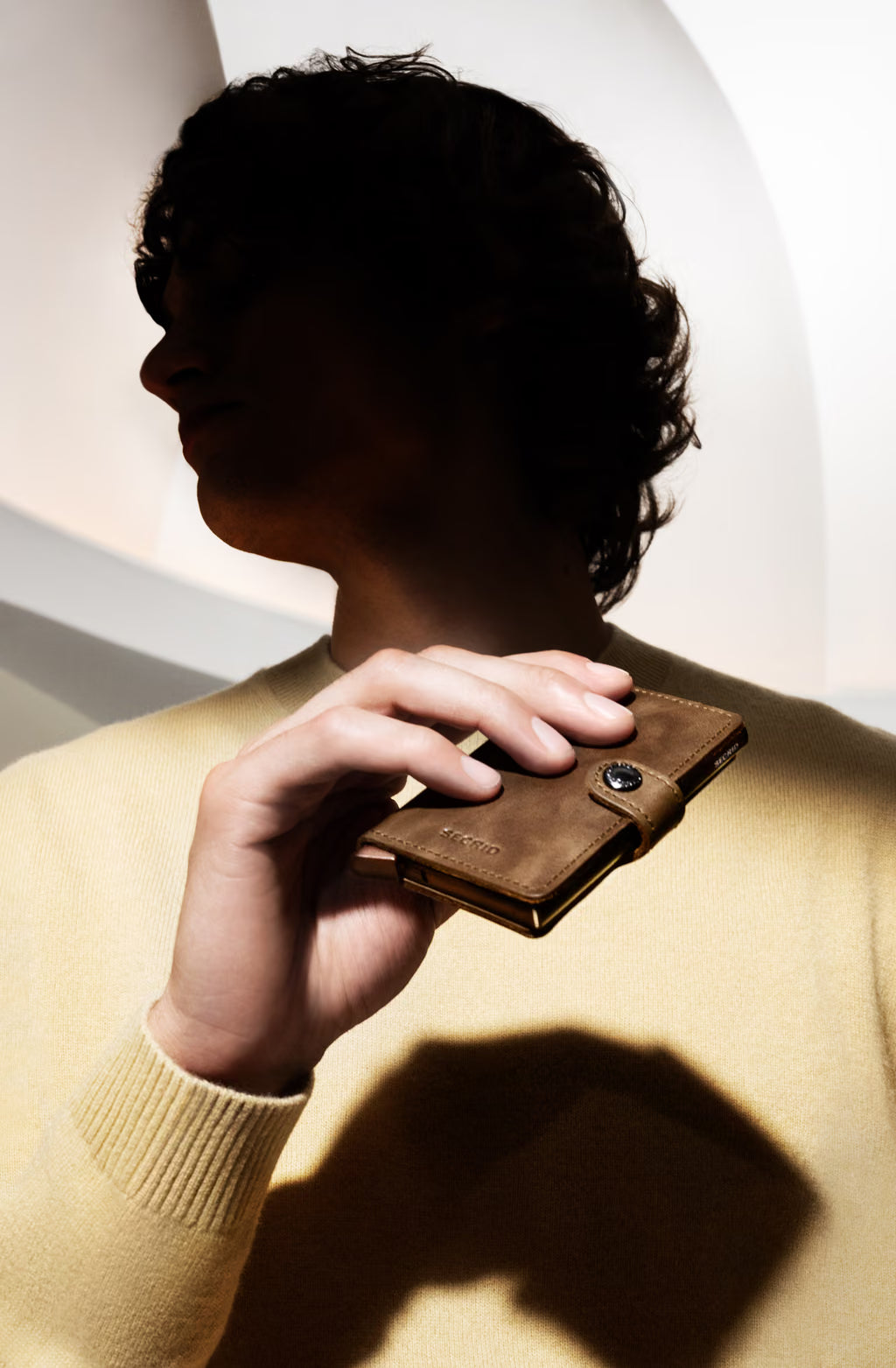 Secrid mini wallet held in hand, dark brown leather with snap button and stitching.