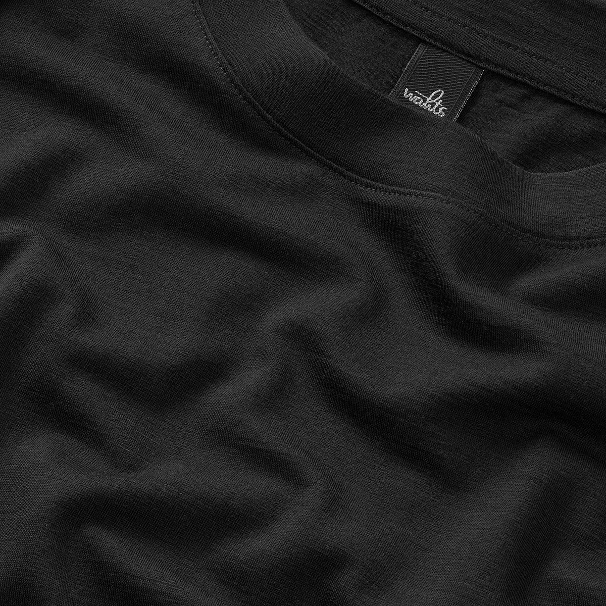 Black virgin wool t-shirt fabric close-up with stitched crew-neck collar and tag