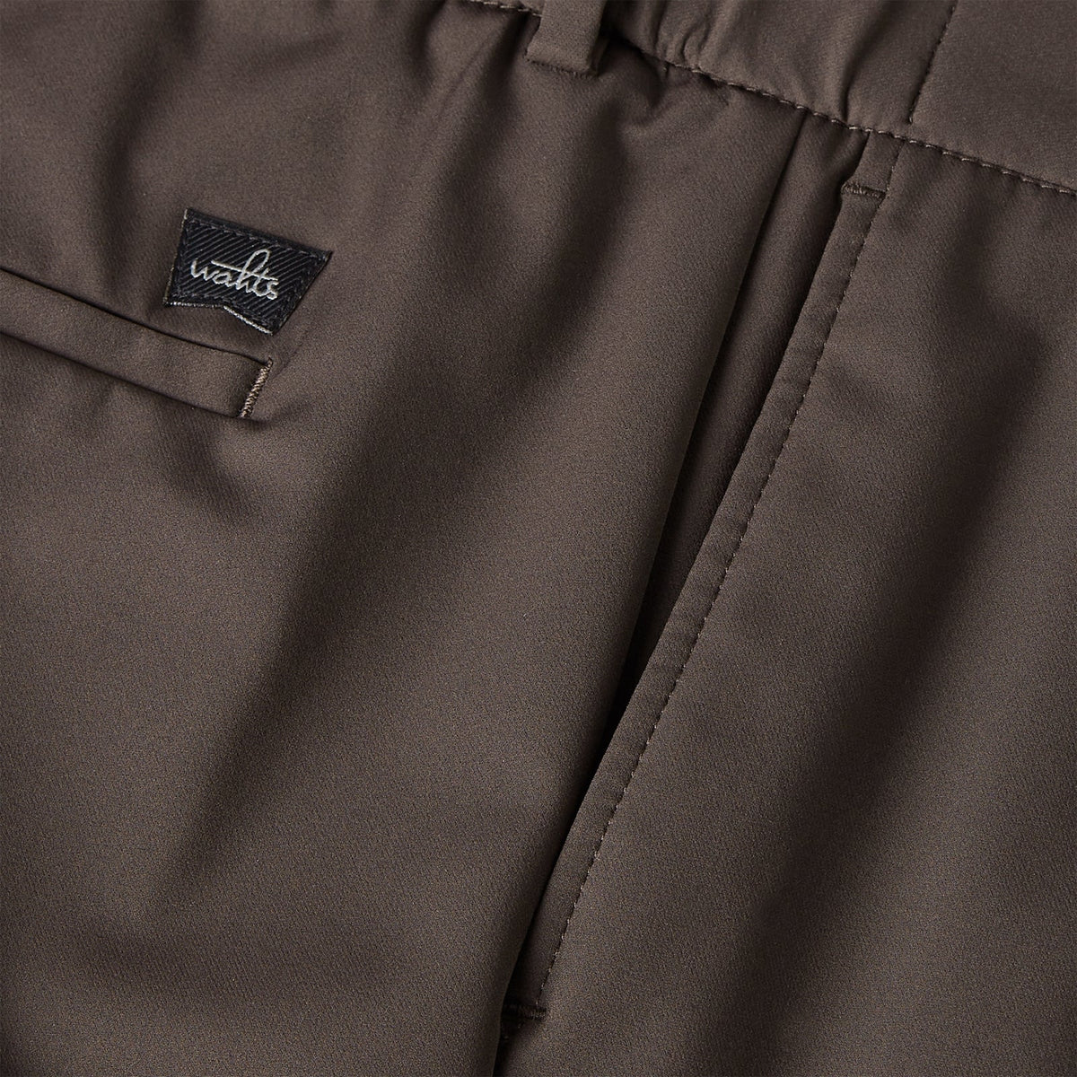 Dark brown trousers with logo label patch and neat stitched waistband detail
