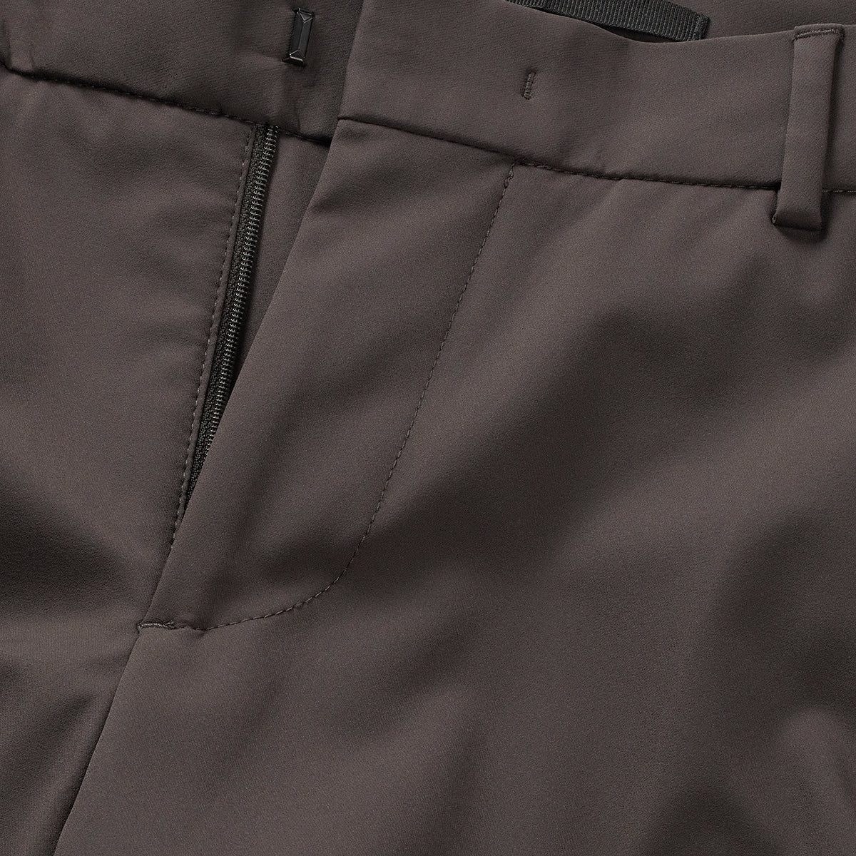 Close-up of dark brown trousers: zip front, stitched seams, and pocket opening