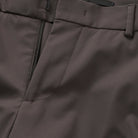 Close-up of dark brown trousers: zip front, stitched seams, and pocket opening
