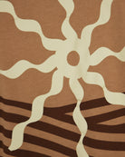 Caramel T-shirt close-up with white sun graphic over dark and light striped pattern.