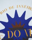 White T-shirt detail of blue sunburst with brown center and gold letters