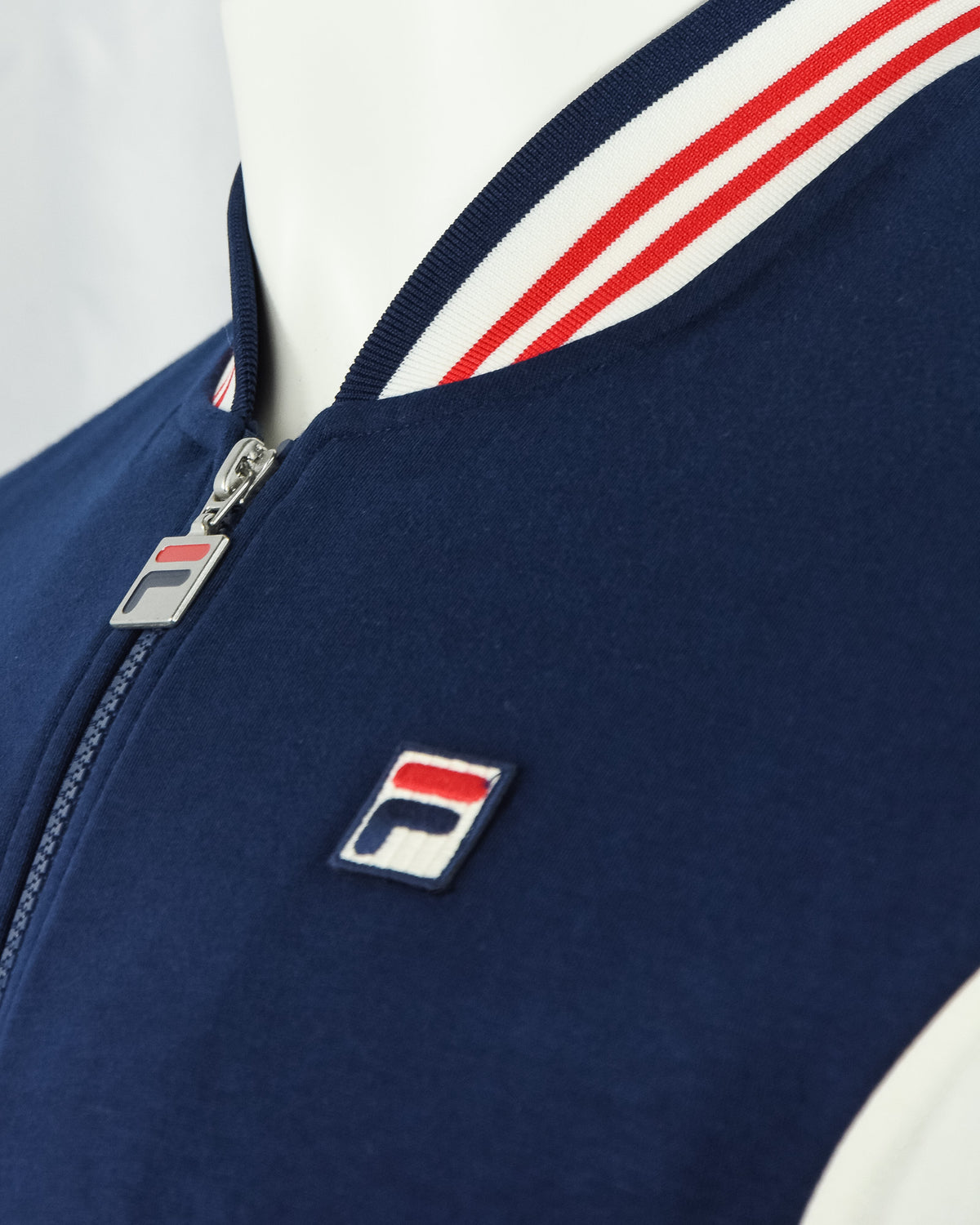 Navy track jacket with silver zipper, logo patch, and red/white shoulder trim