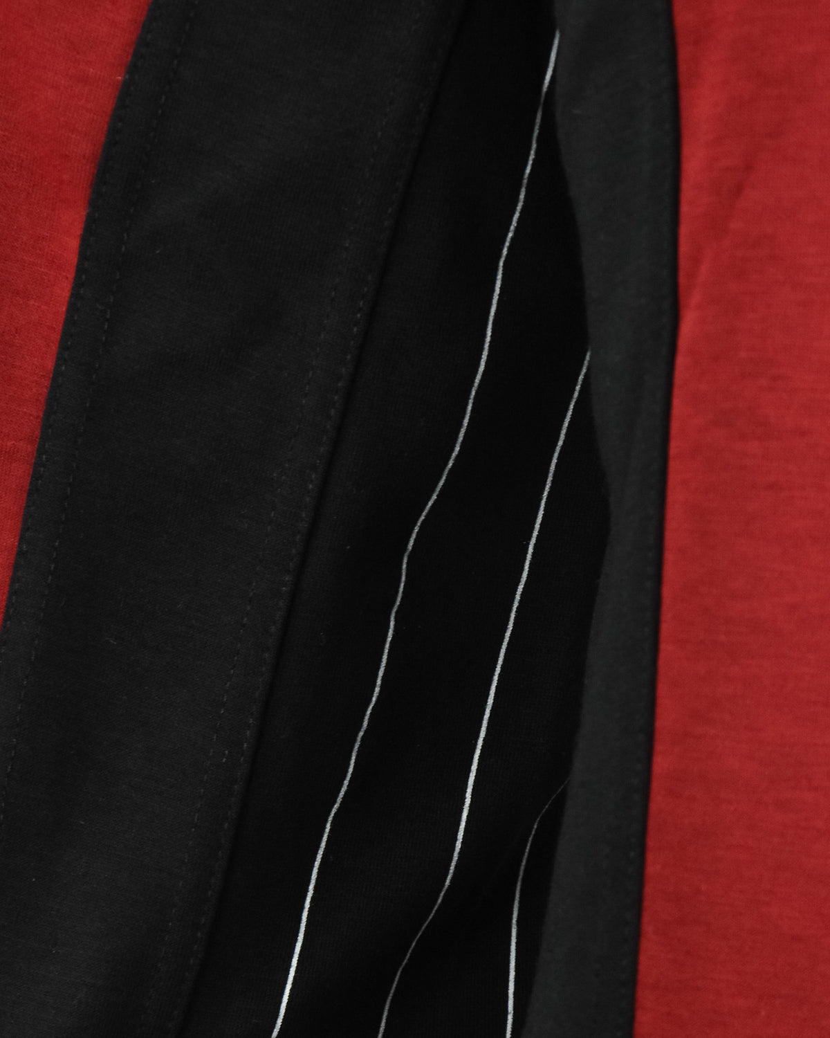 Close-up of black sleeve panel with curved white stripe accents on red fabric.