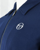 Navy track jacket close-up of zip placket and white logo emblem