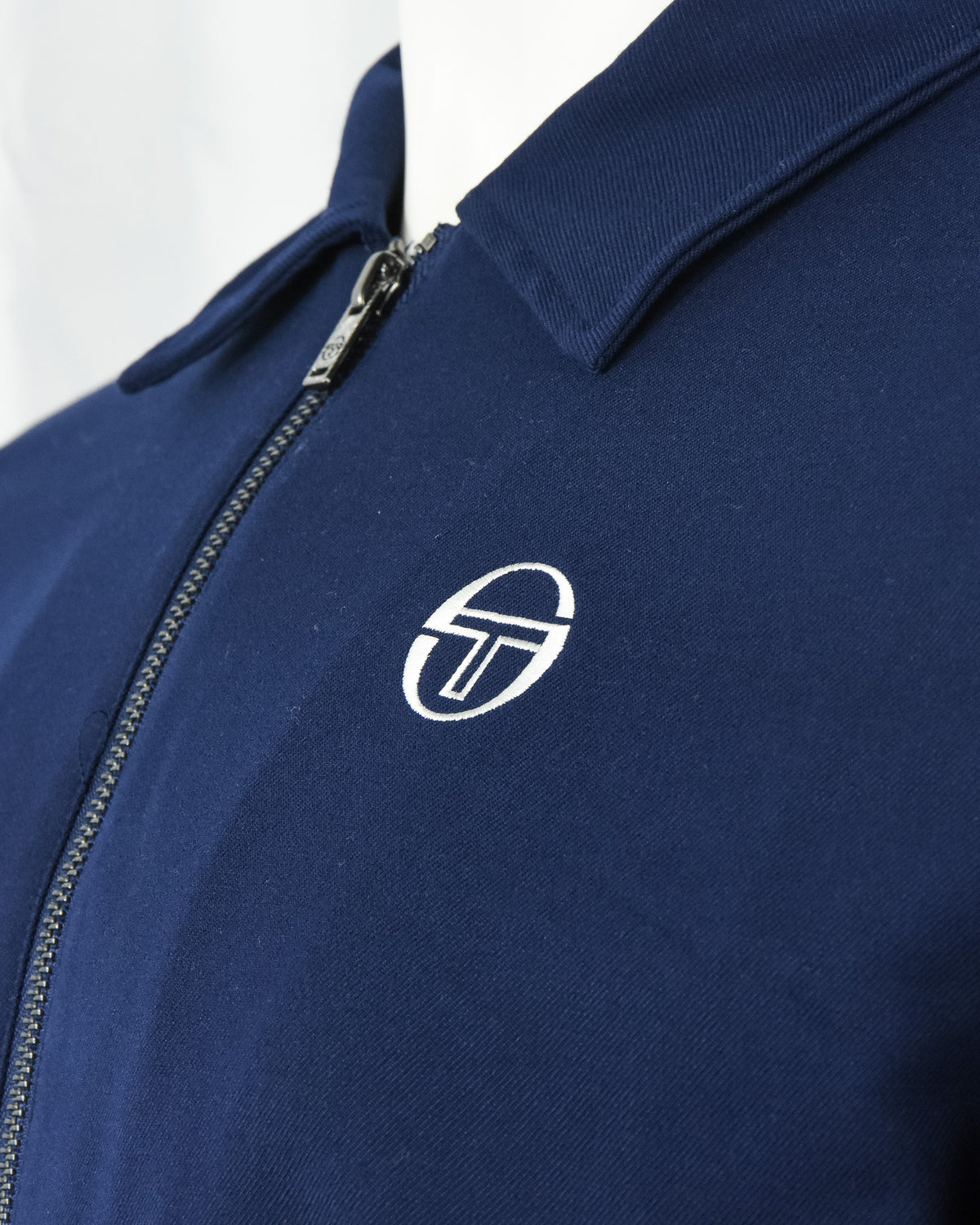 Navy track jacket close-up of zip placket and white logo emblem