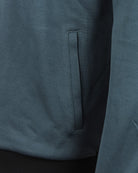 Teal track jacket close-up of front pocket opening and zip placket