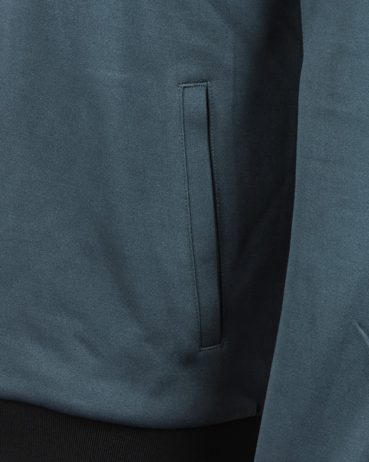 Teal track jacket close-up of front pocket opening and zip placket