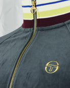 Close-up of dark teal velour track jacket with gold zip and embroidered S logo