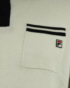 Cream polo chest pocket with black-and-white stripe trim and Fila logo patch.