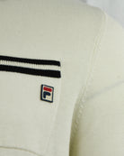 Close-up of cream polo pocket with black stripe trim and Fila logo patch.