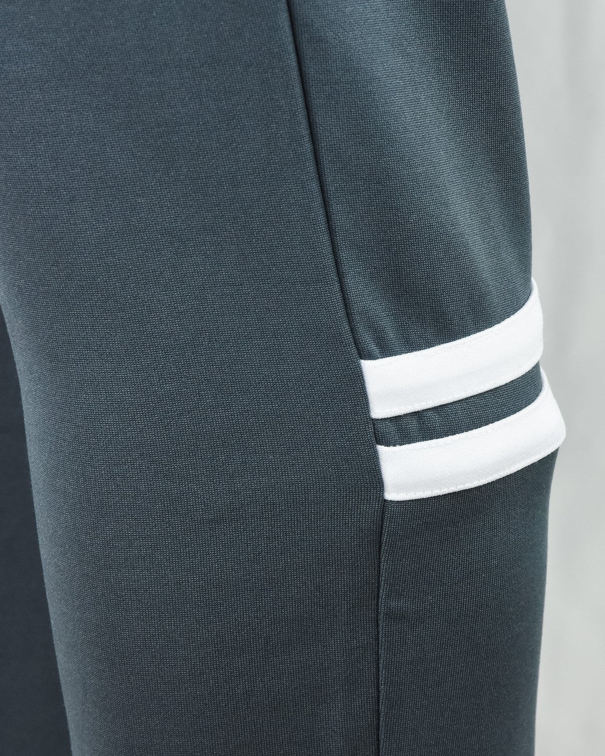 Track pants cuff close-up with dark teal knit and two white stripes