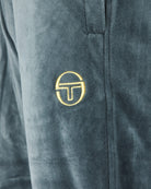 Velour track pants close-up: embroidered gold logo on side panel