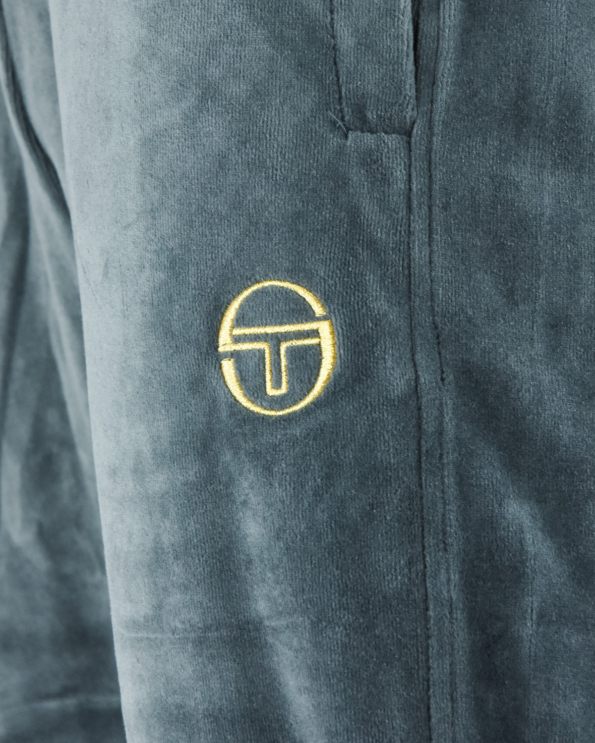 Velour track pants close-up: embroidered gold logo on side panel