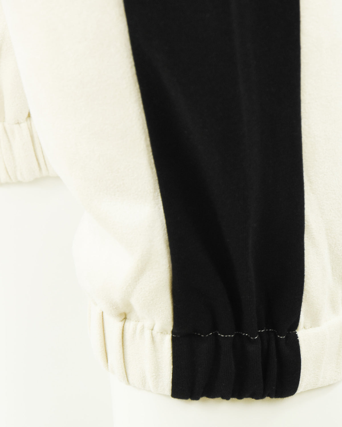 Cream-and-black track pants hem with elastic cuff and stitched finish at ankle