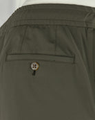 Olive pants close-up: front welt pocket and decorative metal-button closure