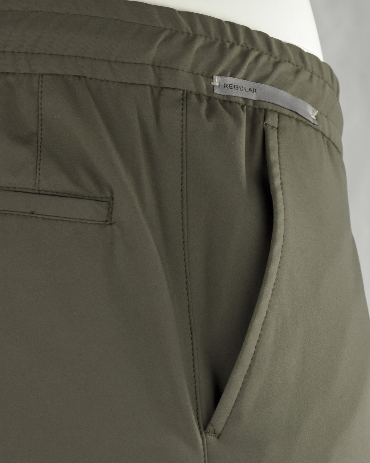 Olive pants close-up: 'REGULAR' label, slanted pocket opening, double-stitched seams