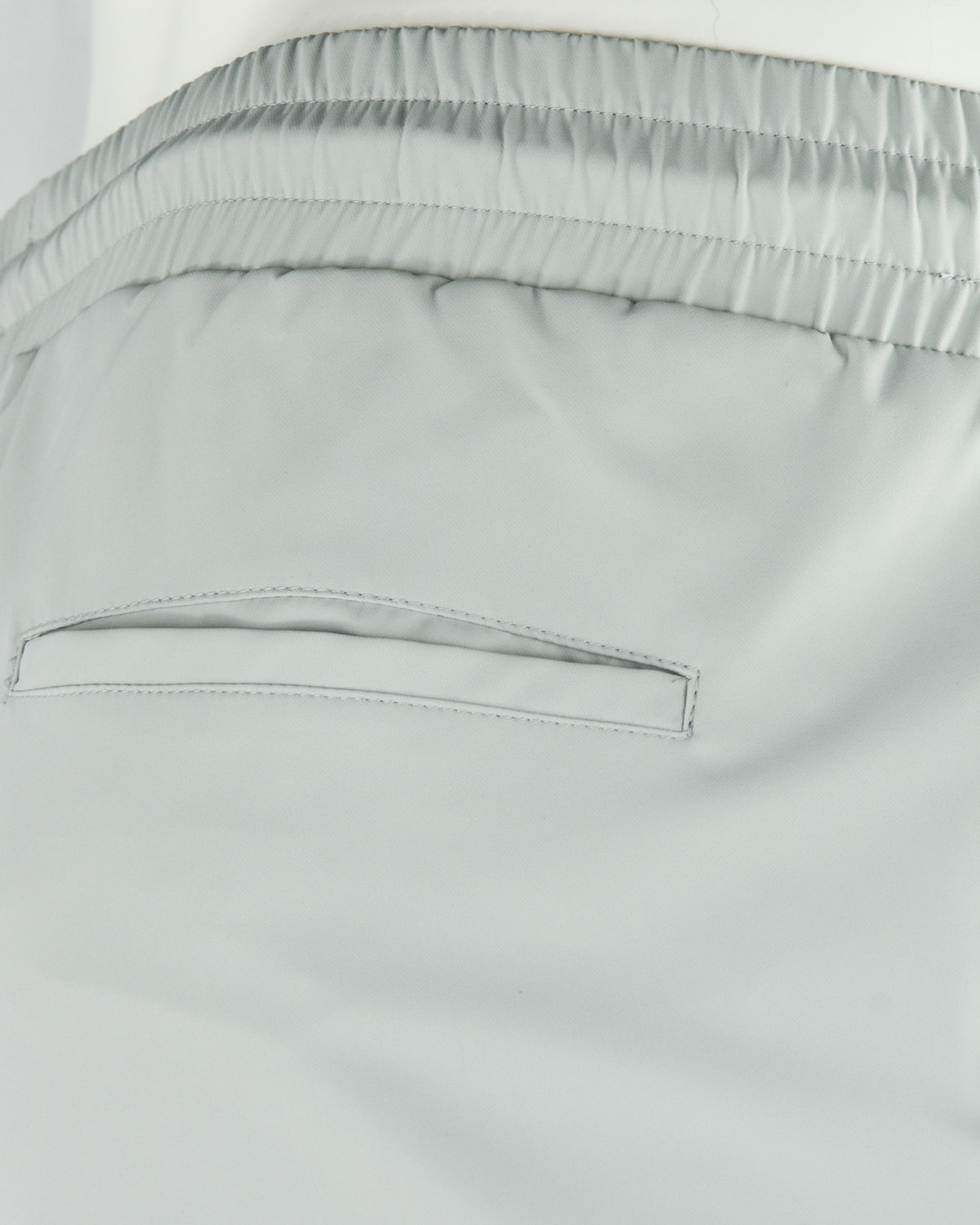 Stone grey tech pants waistband close-up with elastic channel and stitched seams