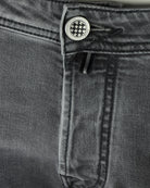 Waistband close-up with logo button and belt loops on dark grey denim jeans