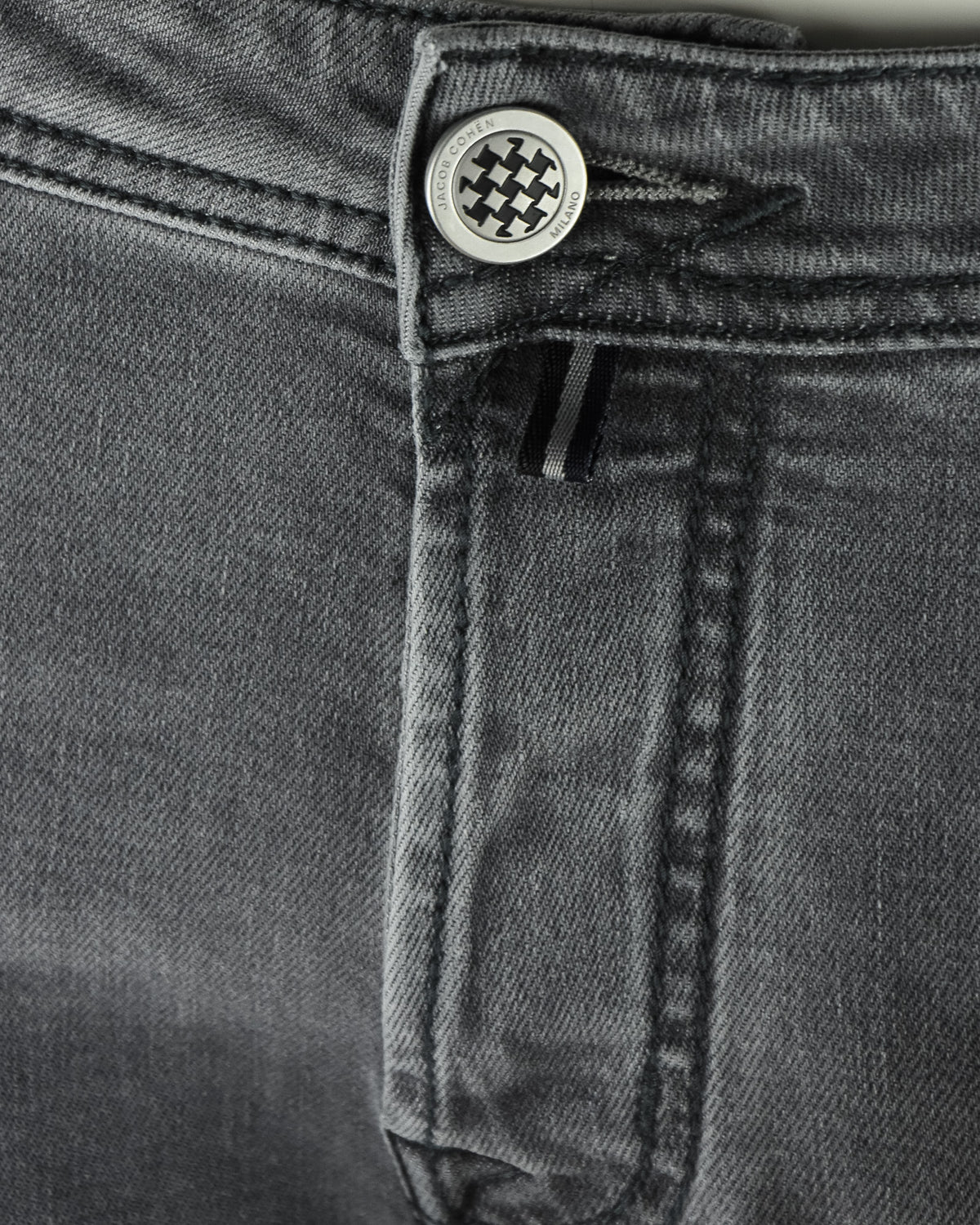 Waistband close-up with logo button and belt loops on dark grey denim jeans