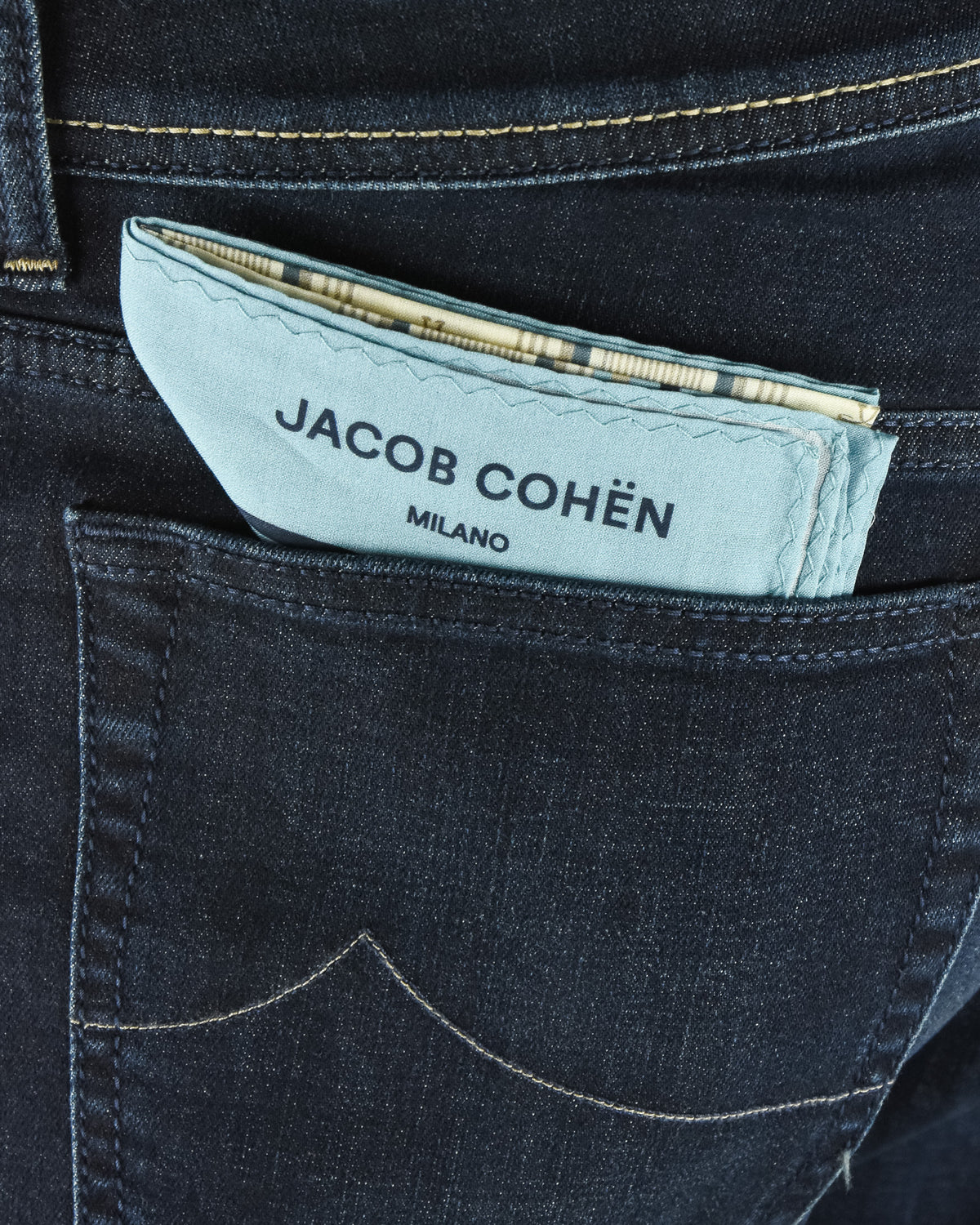Waistband brand patch on dark blue jeans with JACOB COHEN MILANO text.