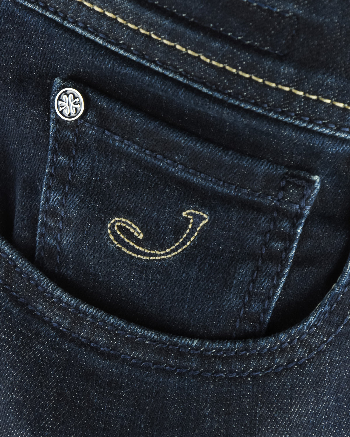 Front pocket with stitched smile graphic and small metal rivet on dark denim.