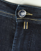 Jeans button closure with circular logo and two gold thread bar details.