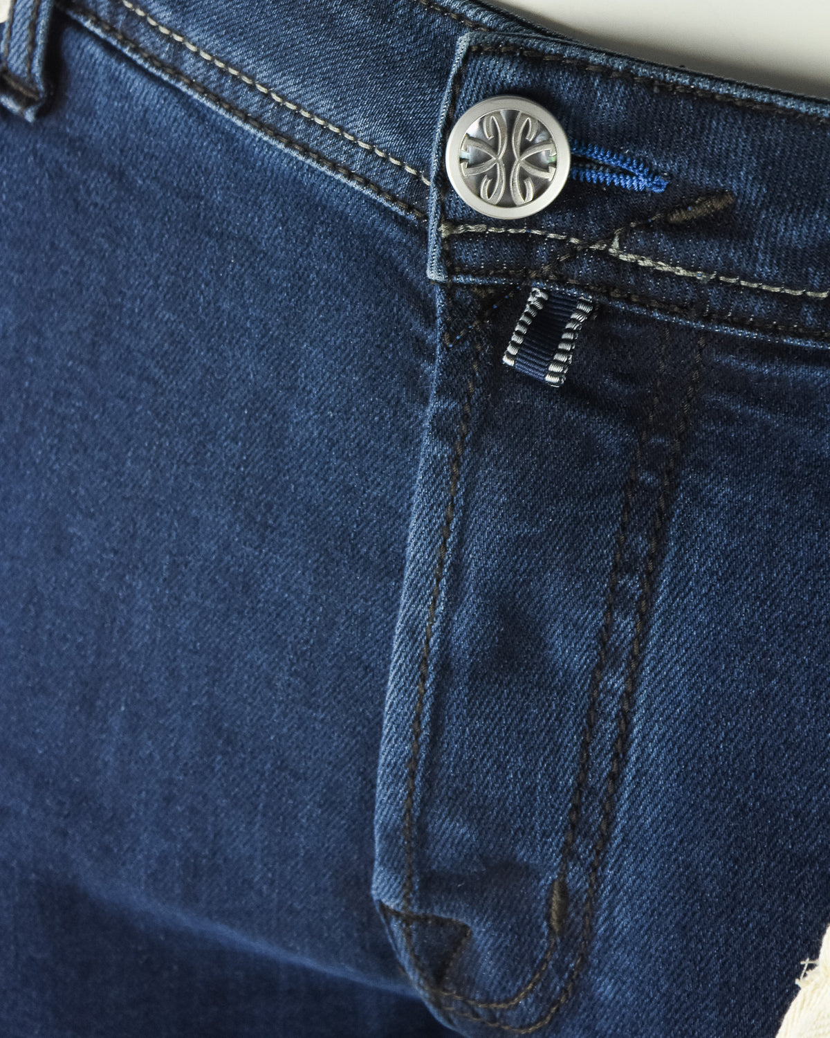 Dark blue denim jeans close-up of button and hidden logo patch detail