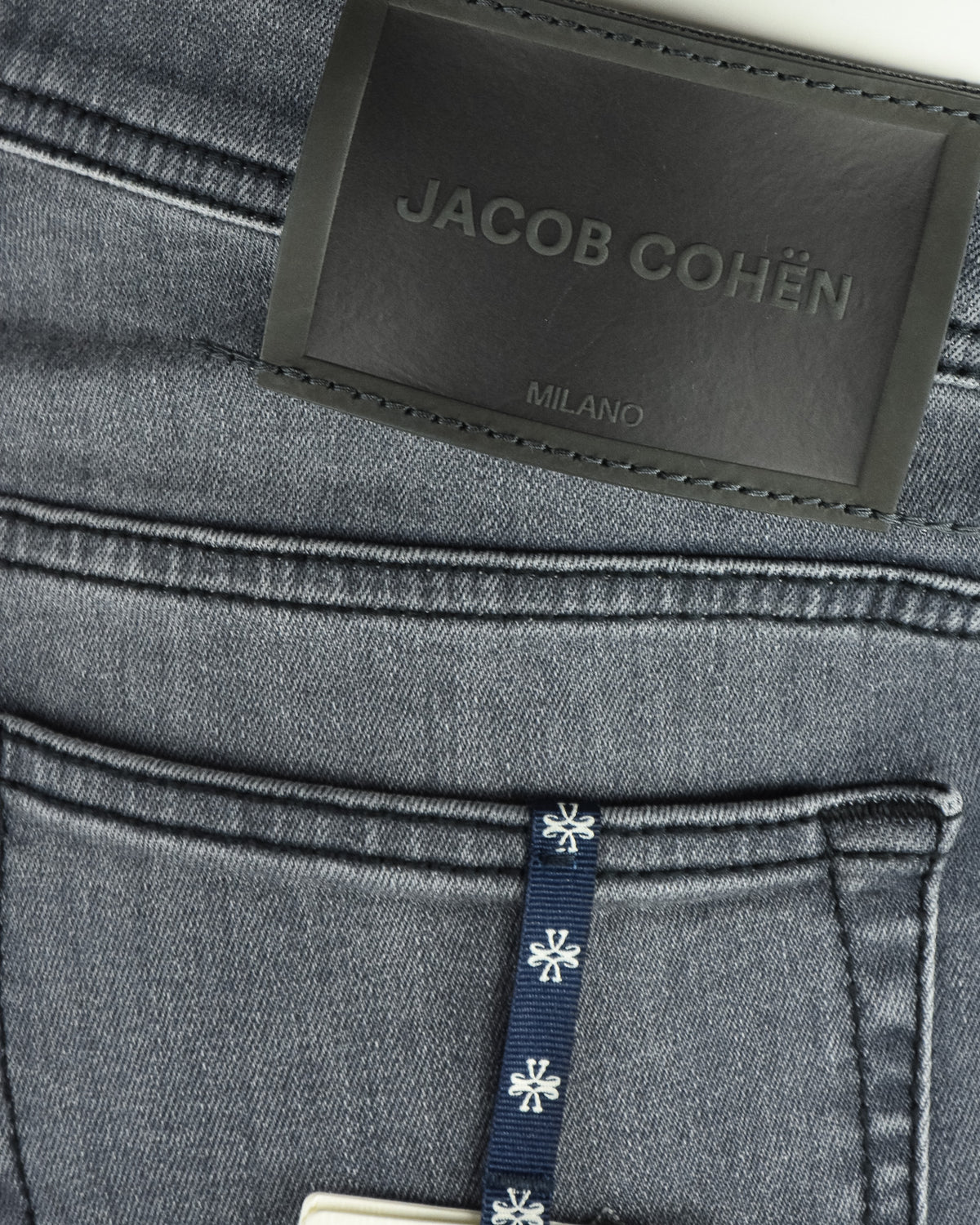 Jacob Cohen Milano waistband label with navy hang tag on grey denim jeans