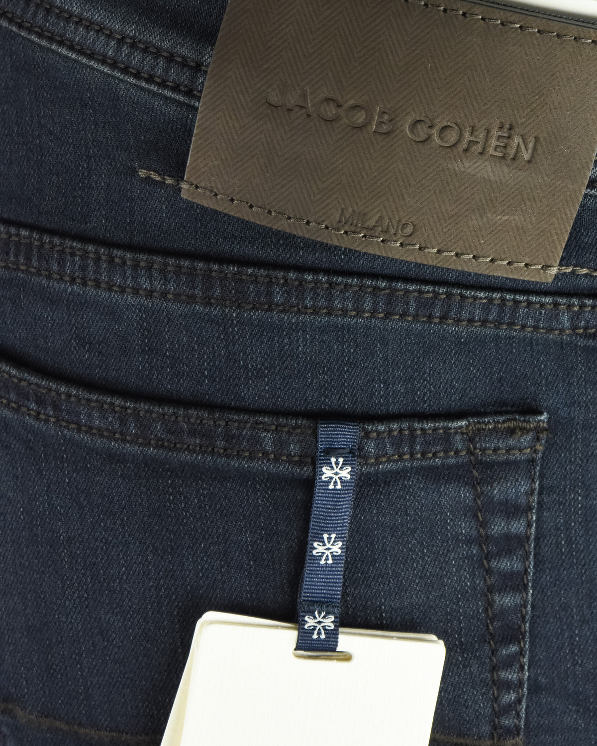 Jacob Cohen leather brand patch on dark blue denim jeans, stitched label close-up.