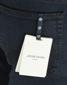 Jacob Cohen size tag hanging from dark blue denim jeans pocket detail.