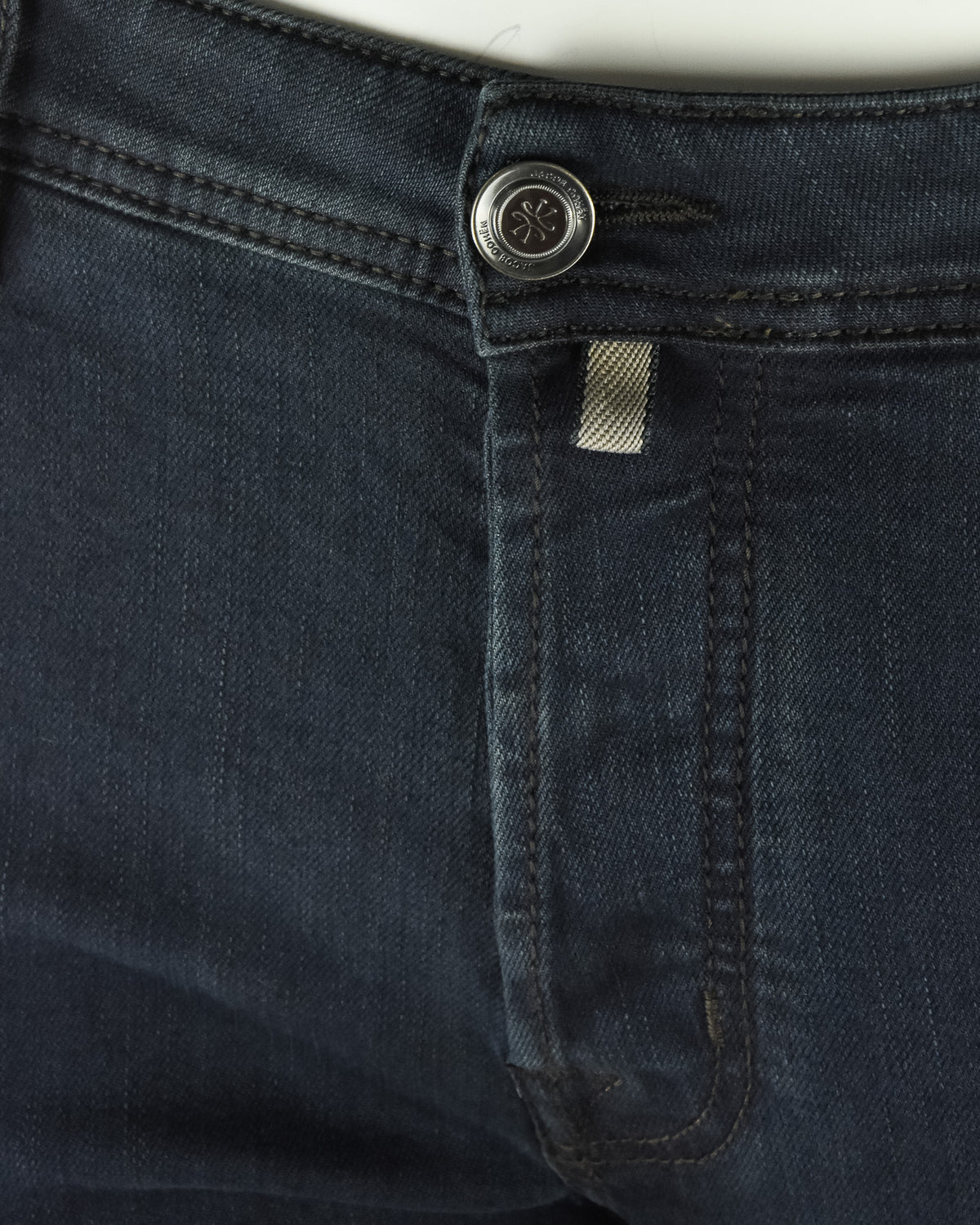 Dark blue stretch denim jeans waist with logo button and inner pocket tab.