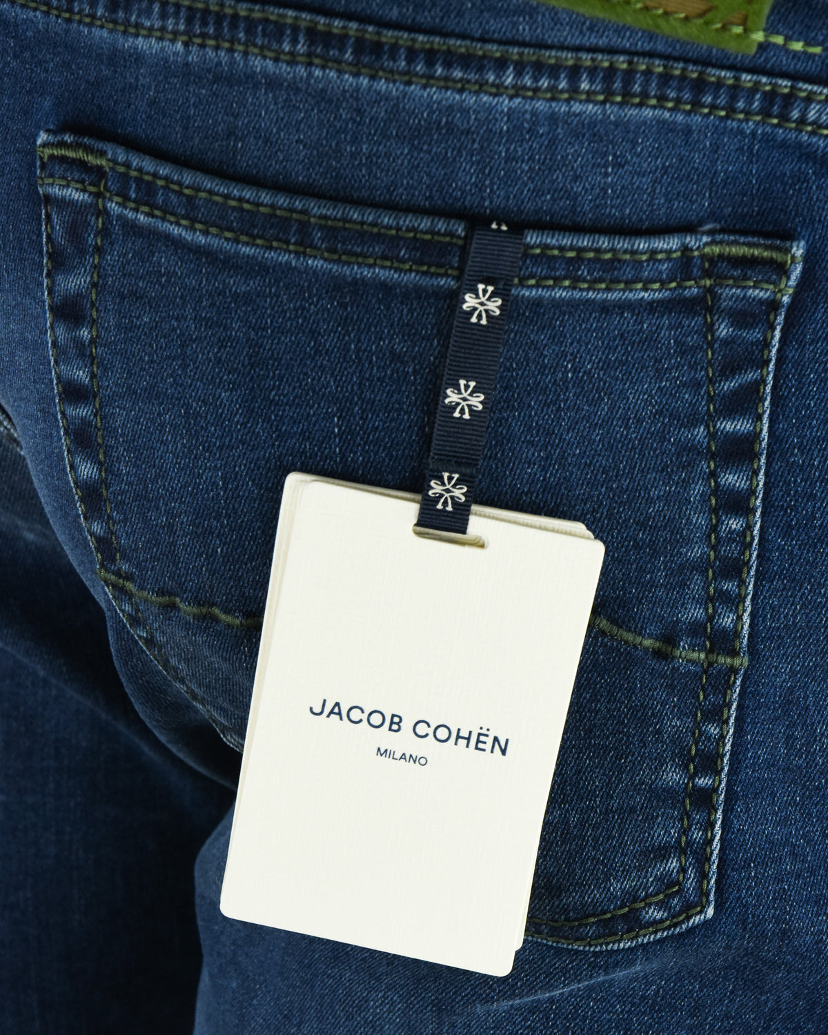 Hanging white retail tag on denim pocket, JACOB COHEN Milano branding visible.