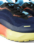 Waterproof running shoe close-up: navy mesh upper with black laces, red logo trim, blue details.